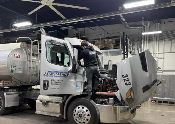 Technician replacing a semi truck windshield on-site in a shop bay