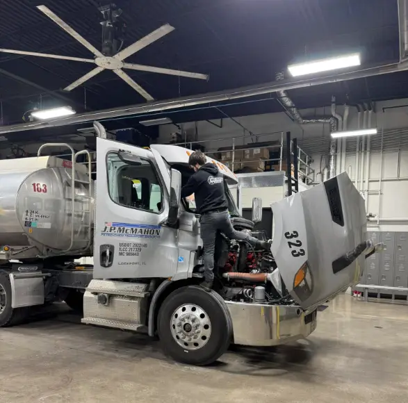 Technician replacing a semi truck windshield on-site in a shop bay